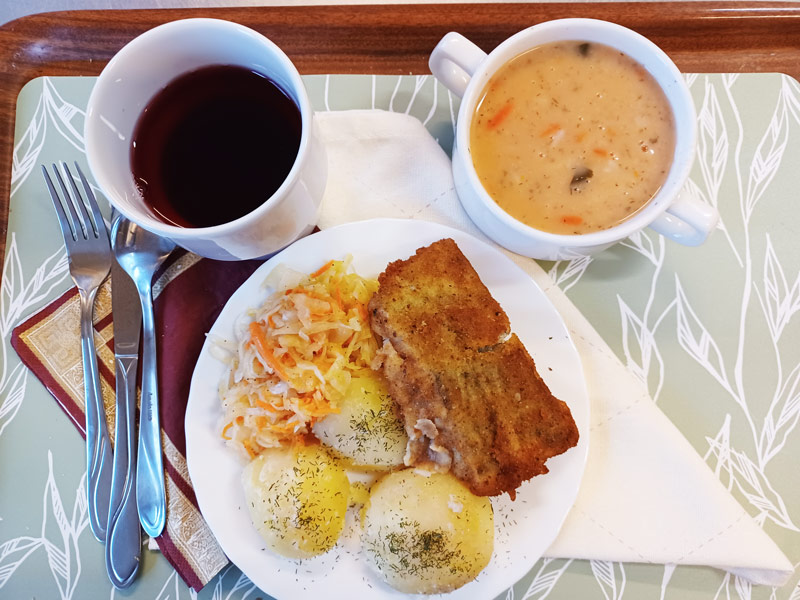 danie obiadowe na białym talerzu i na brązowej tacy, sztućce oraz kubek z zupą i kubek z napojem